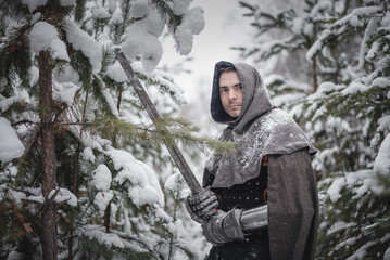 A knight in the armor with the sword in the winter snowy forest.