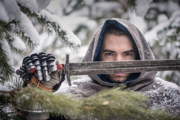 A knight in the armor with the sword in the winter snowy forest.