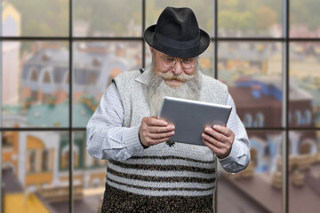 Old caucasian man using digital tablet on window background with view of city buildings.