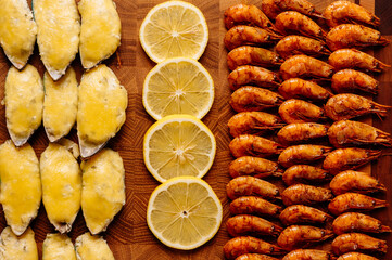 Mussels baked with cheese sauce and sliced lemon and fried shrimps on wooden cutting board close-up