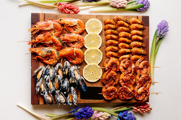 Fried tails of langoustines and fried mussels with sauce and fried shrimps and sliced lemon on wooden cutting board with card and jacinths