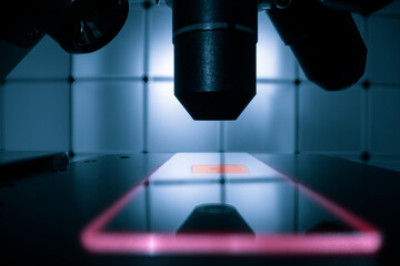 microscope table with a luminous slide and a microscope lens on a dark background