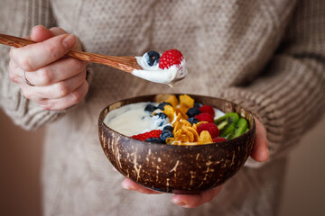 Woman eating healthy breakfast from coconut bowl. Yogurt with corn flakes and berry fruit. Eco...