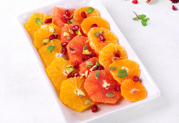 Citrus fruit salad with orange, blood orange, tangerine slices, pumpkin seed, pistachio and pomegranate on the ceramic rectangular plate on the white table. Healthy vegan meal 
