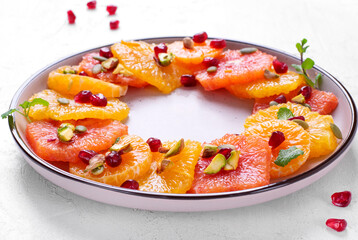 Citrus fruit salad with orange, blood orange, tangerine slices, pumpkin seed, pistachio and pomegranate on the round ceramic plate on the white table. Healthy vegan meal 