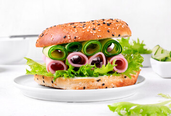 Bagel sandwich with ham and cucumber rolls, lettuce and cream cheese on the white table