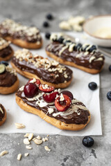 Eclairs with chocolate topping, nuts and berries. Chocolate, nut, banana, cherry and blueberry eclairs. Dessert on a plate. Top view