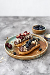 Eclairs with chocolate topping, nuts and berries. Chocolate, nut, banana, cherry and blueberry eclairs. Dessert on a plate. Top view