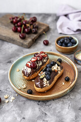 Eclairs with chocolate topping, nuts and berries. Chocolate, nut, banana, cherry and blueberry eclairs. Dessert on a plate. Top view