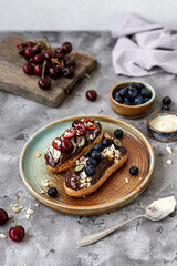 Eclairs with chocolate topping, nuts and berries. Chocolate, nut, banana, cherry and blueberry eclairs. Dessert on a plate. Top view