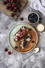 Eclairs with chocolate topping, nuts and berries. Chocolate, nut, banana, cherry and blueberry eclairs. Dessert on a plate. Top view