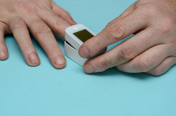 An adult male holds a pulse oximeter on his index finger.