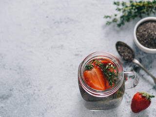 View from above chia water in mason jar with strawberry and thyme on gray cement background. Chia infused detox water with berries. Copy space for text. Healthy eating, drinks, diet, detox concept