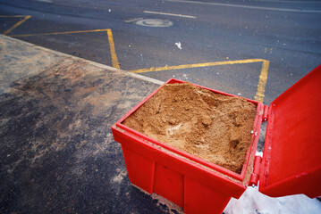Grit bin with sand material for improve traction on snowy and icy sidewalk at bus stop, road maintenance in winter season. Plastic grit container, spread sand to prevent slipping on city street