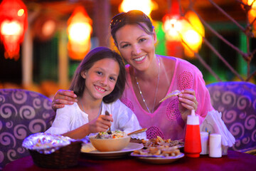 Happy mother and daughter eating in cafe together