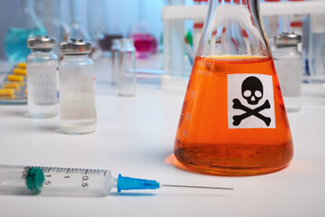 Orange toxin flask and syringe - lab photo. Orange poisonous liquid inside chemical retort. Syringe for death injection on a desk surface. Colored liquids inside chemical flasks, retorts, test-tubes.