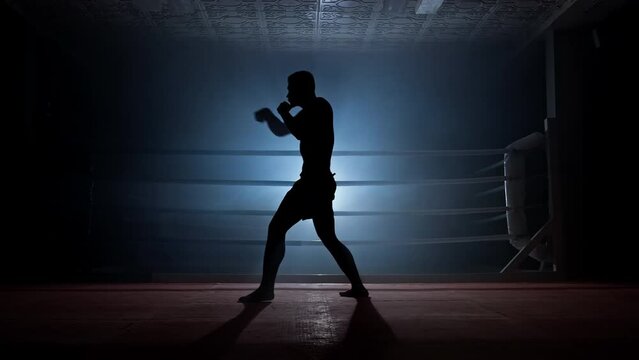 Young man practicing shadow boxing in smoky gym. Silhouette of professional fighter training shadow fight. Strength and motivation. Sport concept. Full length in 4K, UHD