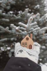 Naklejka premium A model of an eco-friendly wooden house in the hands on a winter background.