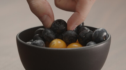 man hand take blueberries and physalis from black bowl