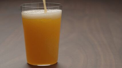 pour orange lemonade in tumbler glass on wood table with copy space