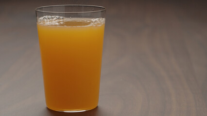 pour orange lemonade in tumbler glass on wood table with copy space