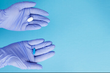 Woman hands in medical gloves giving two big pills. Blue and white. Make your selection
