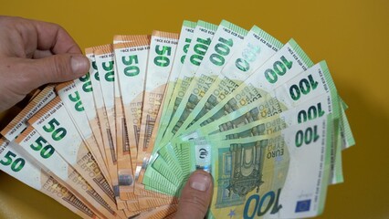 hands count money euro banknotes 100 and 50 € on a yellow background