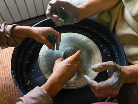 The master of the pottery craft teaches the student to work on the potter's wheel. Creating dishes from clay. Selective focus.