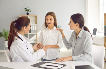 Parent and child talking to family doctor. General practitioner holding kid by hands during...