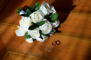 Wedding rings on a wooden table in the sun next to a wedding bouquet of roses