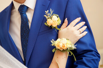 The hand of the bride with a boutonniere rests on the forearm of the groom in a blue suit with a...