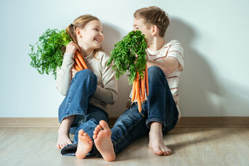 Happy smiling brother and sister with  bunch of orange carrots