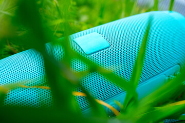 A close-up of a blue wireless music speaker lying among the dense green grass. Modern devices for...