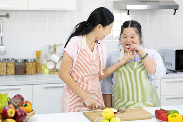 mother feeding apple to down syndrome teenage girl or her daughter in the kitchen