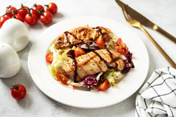 Grilled chicken fillet with vegetables in a white plate on a light gray culinary background. Dietary poultry breast on the kitchen table closeup