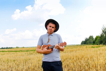 Artist. Young beautiful caucasian man playing ukulele outside. Handsome hipster guy plays ukulele...