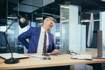 Tired worker businessman working in the office sitting at the computer, the man has severe back pain