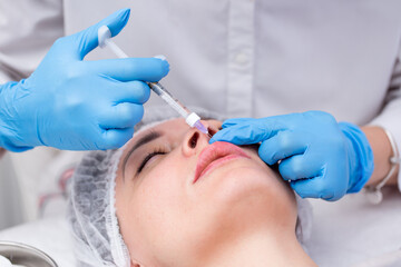 Lip augmentation. Beautician injects hyaluronic acid into the lips of a girl with a syringe. The cosmetologist doctor performs the procedure in the cosmetology office. Plastic surgery.