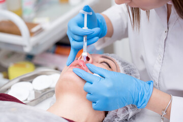 Lip augmentation. Beautician injects hyaluronic acid into the lips of a girl with a syringe. The...