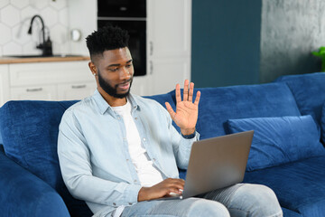 Video call. Cheerful attractive multiracial guy using computer app for video communication. Smiling guy looking and waiving into the camera, greeting, talking online