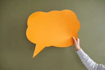 Hand of unknown woman having idea holding empty speech bubble on green background. Young woman holding orange speech bubble in shape of cloud on khaki background. Copy space.