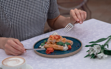 The girl is having breakfast with Belgian waffles with salmon pieces and sauce.