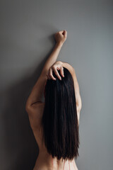 A naked woman with long hair stands against the wall