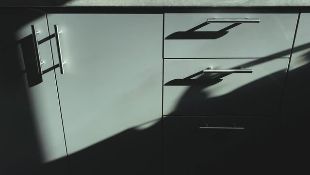 Close-up view of kitchen grey cabinets with metallic handles, in the sunlight.