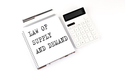 Notepad with text LAW OF SUPPLY AND DEMAND with calculator and pen. White background. Business concept