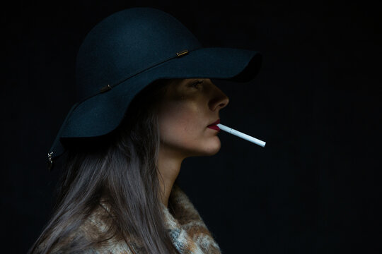 A woman in a hat smokes a cigarette on a dark street