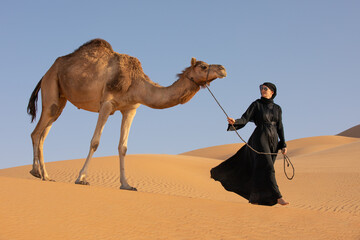 Young woman in Emirati national dress (abaya) with a camel in Empty Quarters desert dunes. Abu...