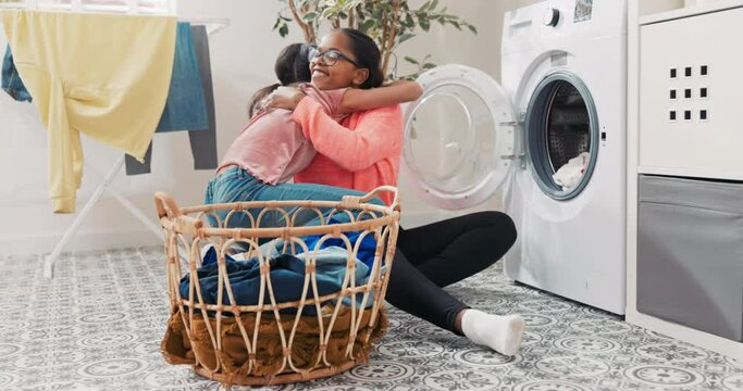 Joyful woman spends time together with daughter while doing household chores, they sort laundry together, throw colorful items into the washing machine little girl hugs mother who thanks her for help