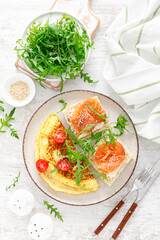 Omelette or omelet, fresh arugula and tomato salad and toasts with butter and salted salmon. Breakfast. Top view