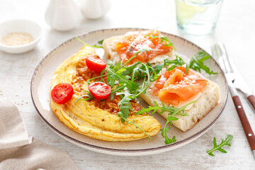 Omelette or omelet, fresh arugula and tomato salad and toasts with butter and salted salmon. Breakfast